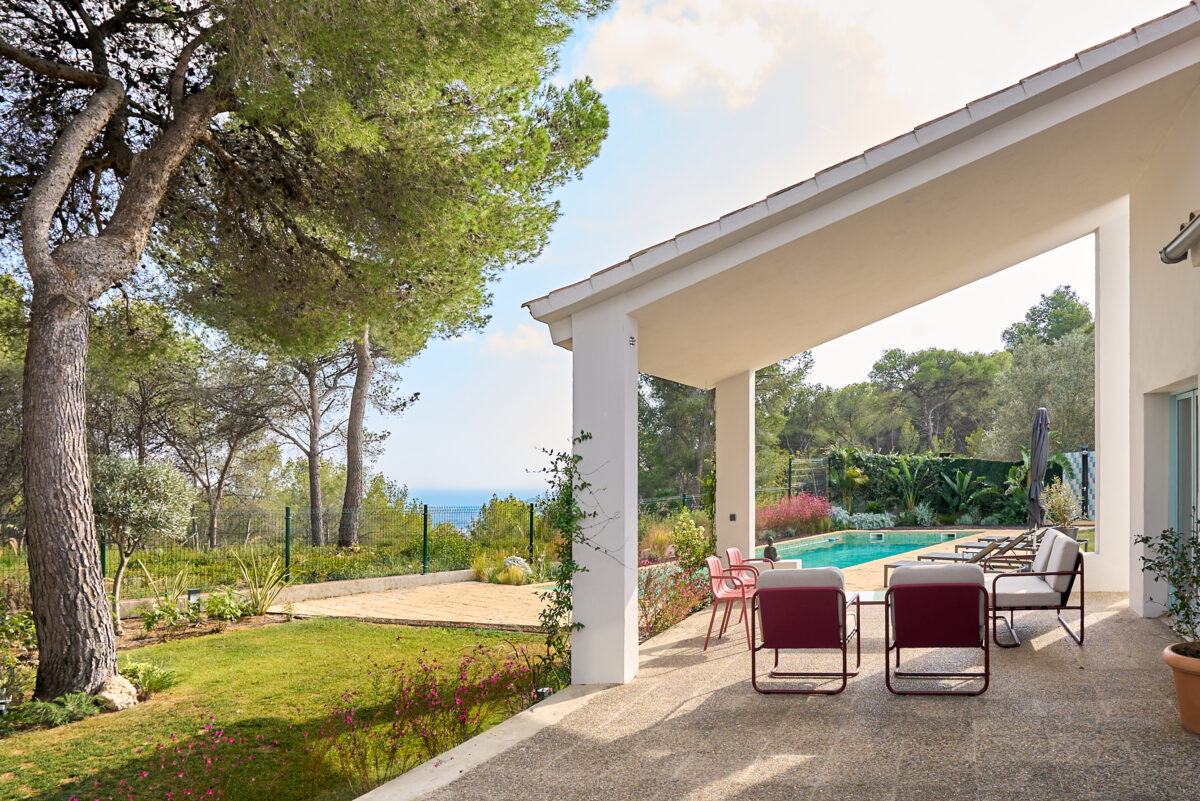 Shaded terrace with red chairs overlooking the garden and swimming pool at Casa Brisa near Sitges